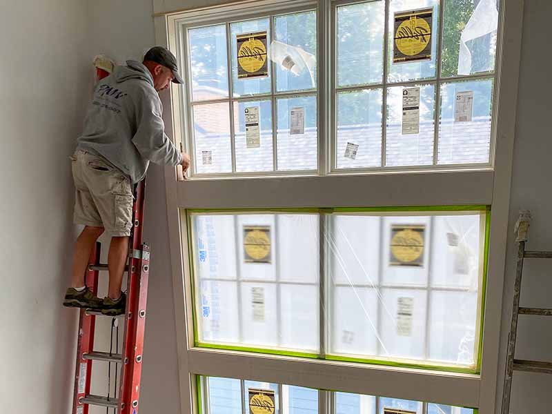 a PMV employee on a ladder painting tall windows