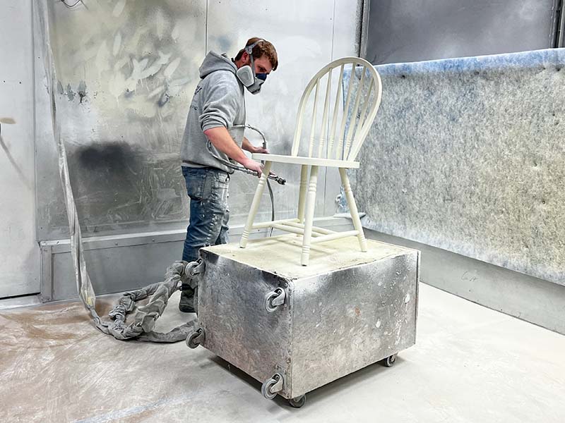 a PMV employee painting a chair in the spray booth