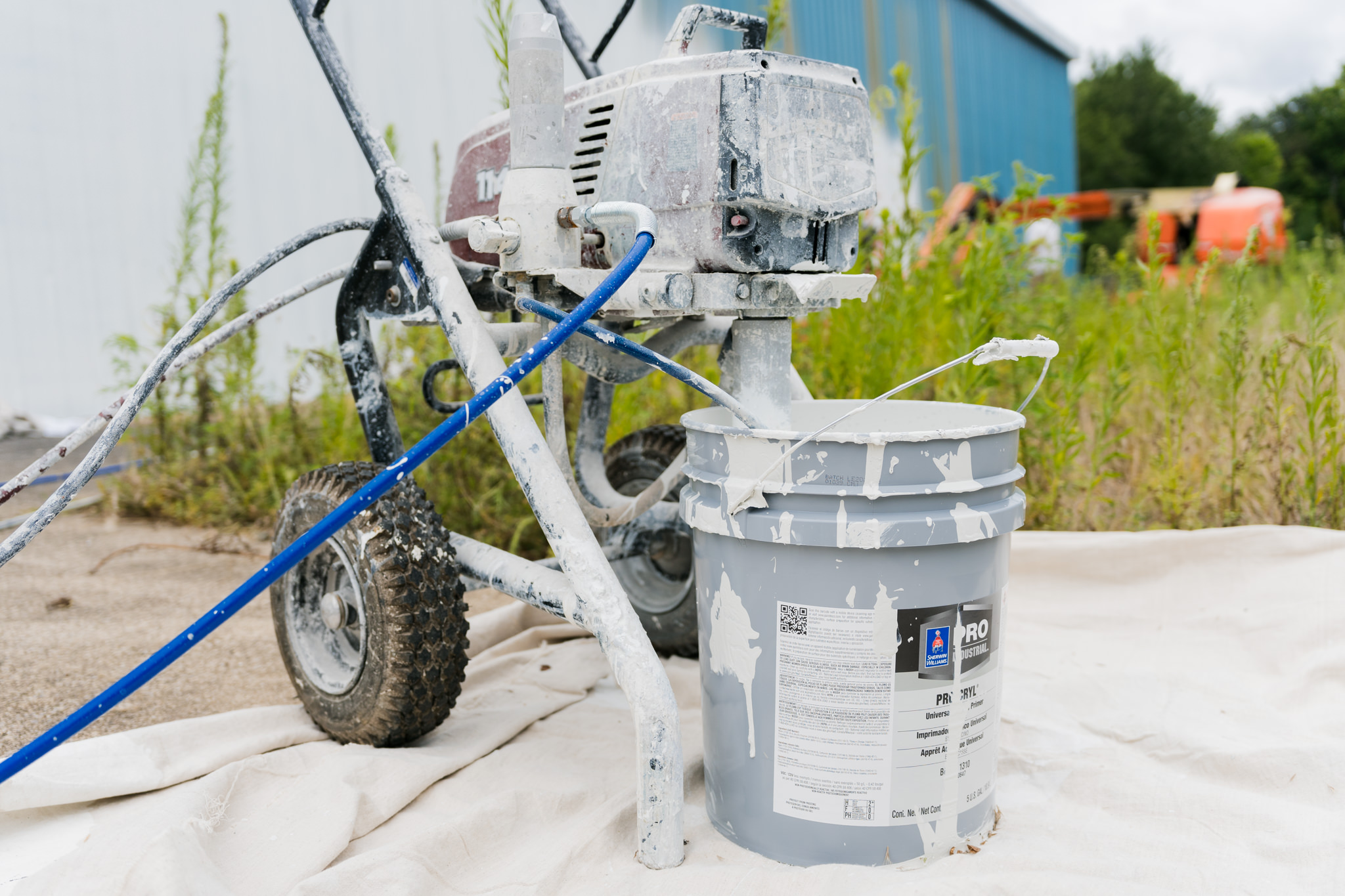 paint sprayer outside using a large 5 gallon bucket of paint.